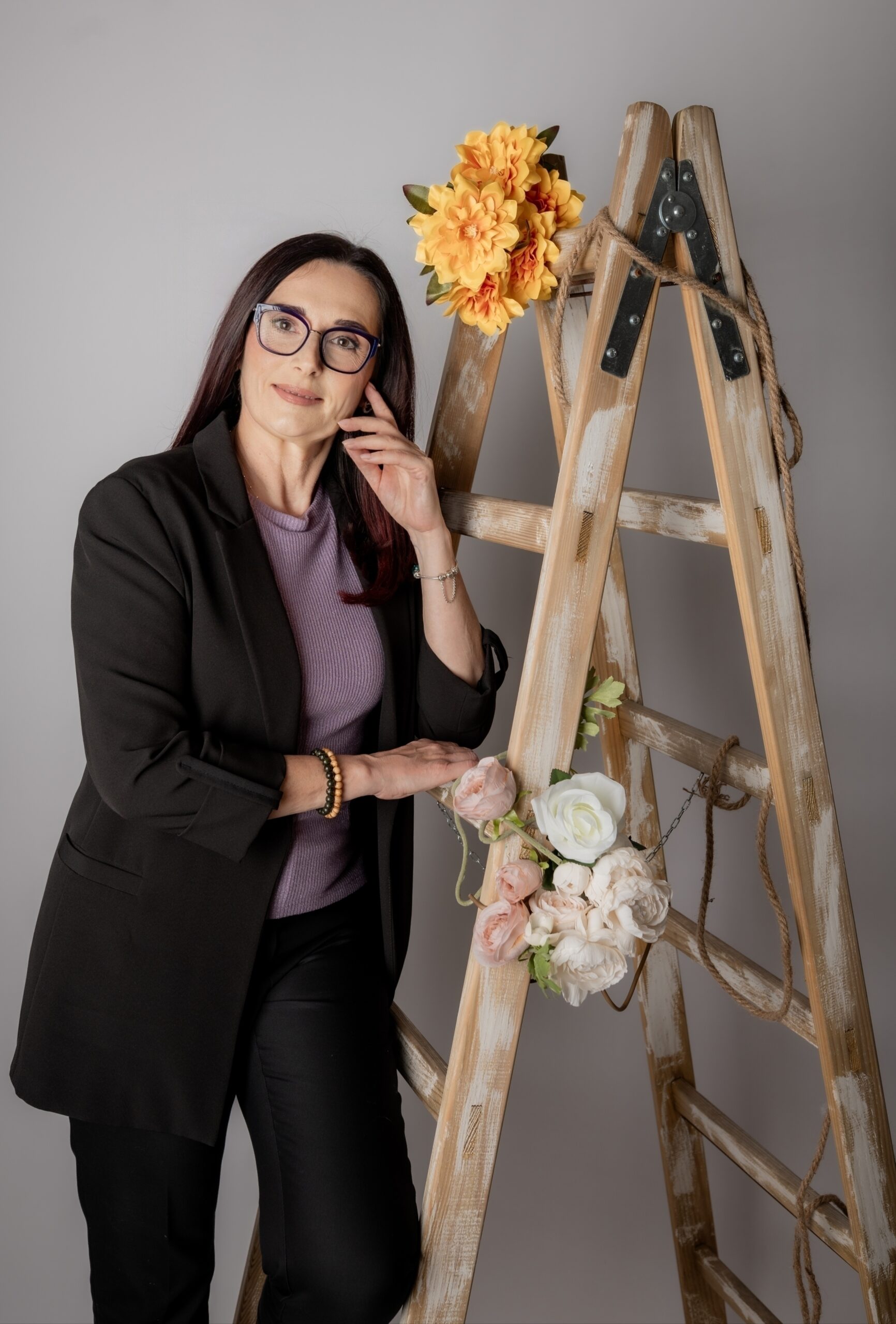 SanVitalis – terapeutica Sandra Knez, smirena i nasmiješena, oslonjena uz skale ukrašene nježnim cvjetovima, u trenutku topline i autentičnosti.